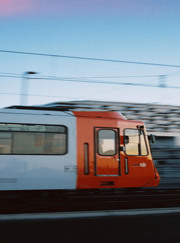 Vista lateral de un tren naranja y blanco que se desplaza a gran velocidad, con desenfoque de movimiento.