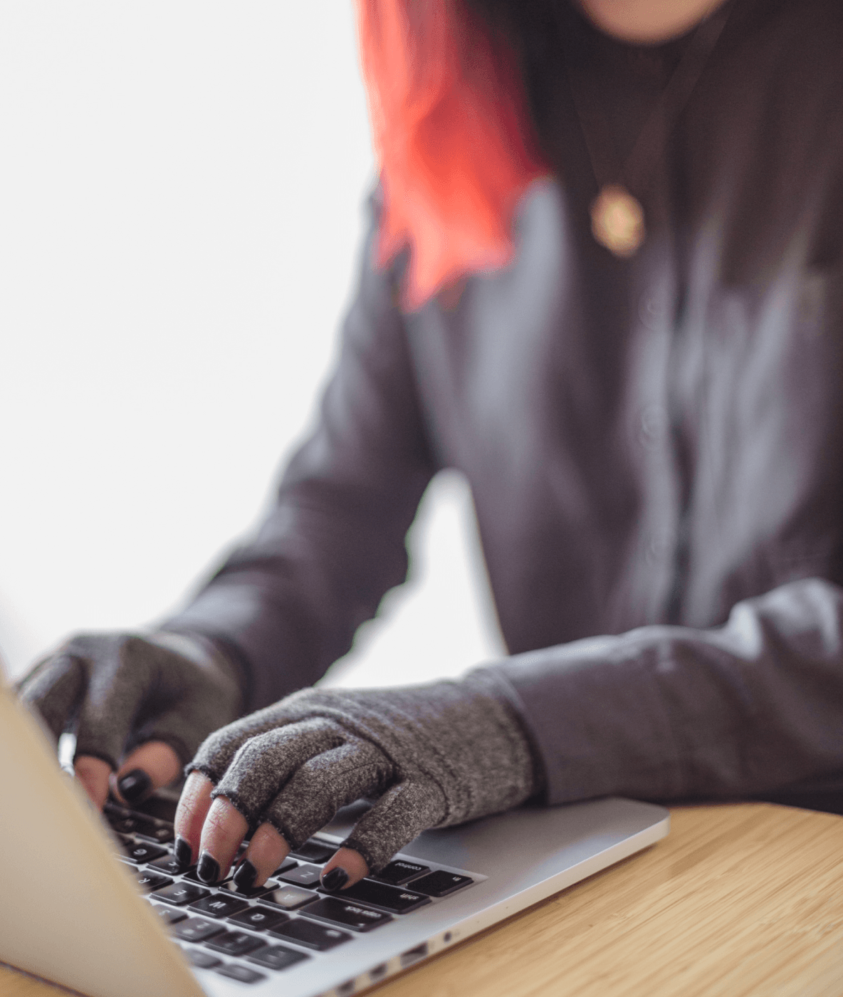 Une personne asiatique en situation de handicap et non binaire tape sur un ordinateur portable tout en portant des gants de compression. Les mains et le clavier sont le point focal.