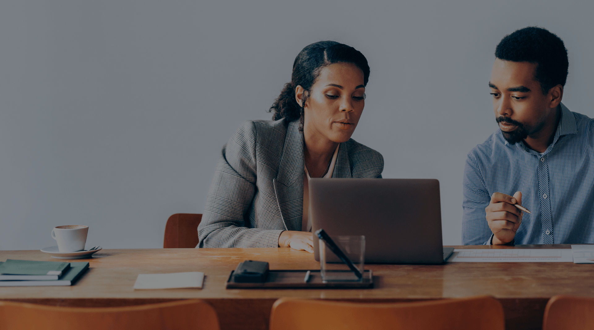 Image of two people working at a table next to a laptop.