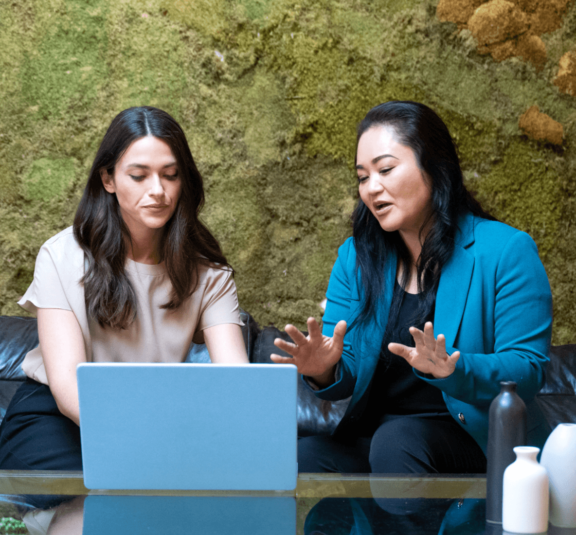 2人の女性がノートパソコンの前に座って話し合っている画像。