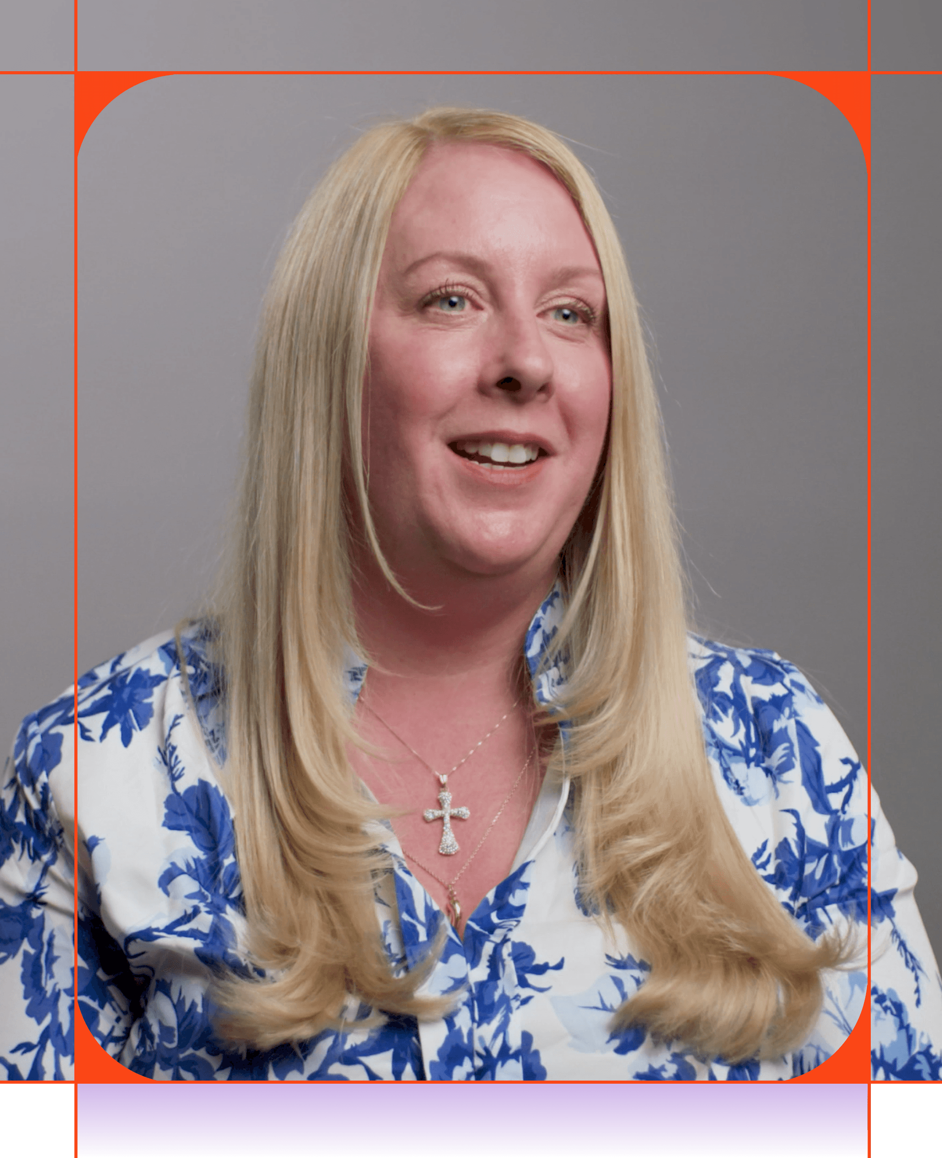 Una mujer sonriente con el pelo largo y rubio, que lleva una blusa floral blanca y azul y un collar con una cruz.