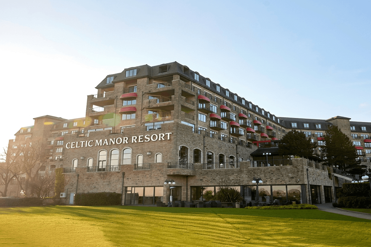 The Celtic Manor Resort, a large stone building with many balconies and red awnings, viewed from a green lawn.
