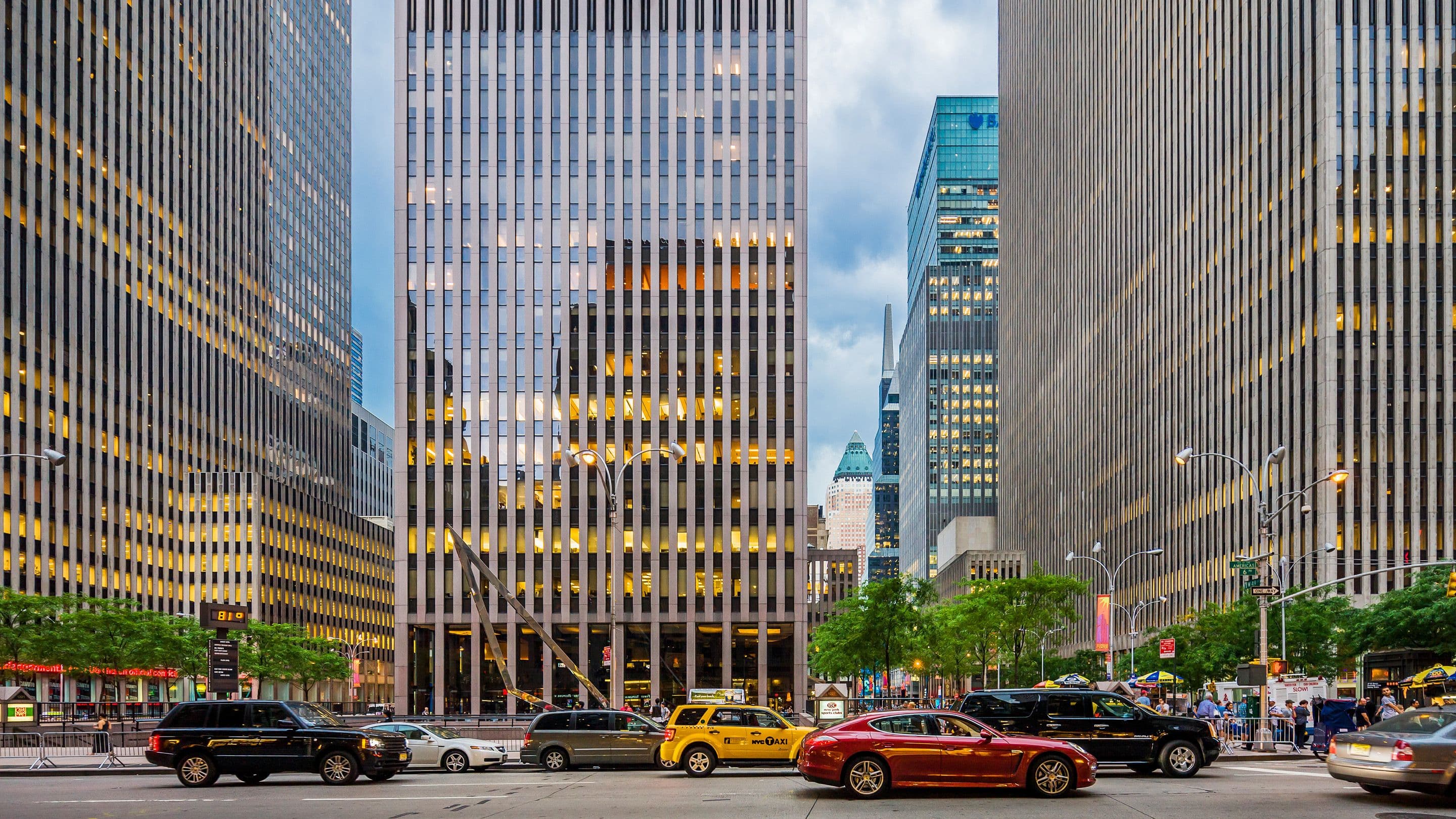 A city street with cars and pedestrians, framed by tall skyscrapers.
