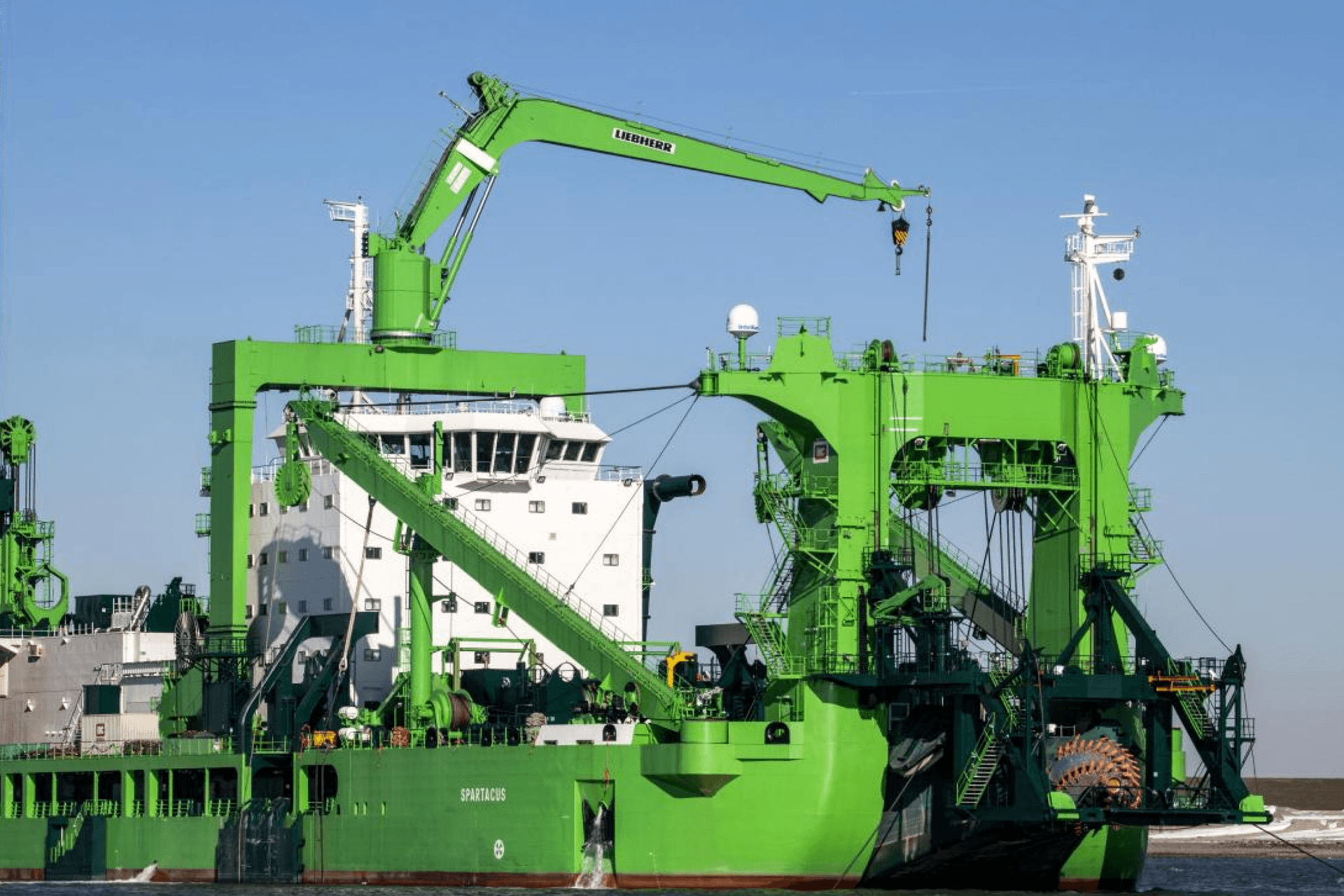 A large green and white cutter suction dredger named "Spartacus" with a prominent crane.