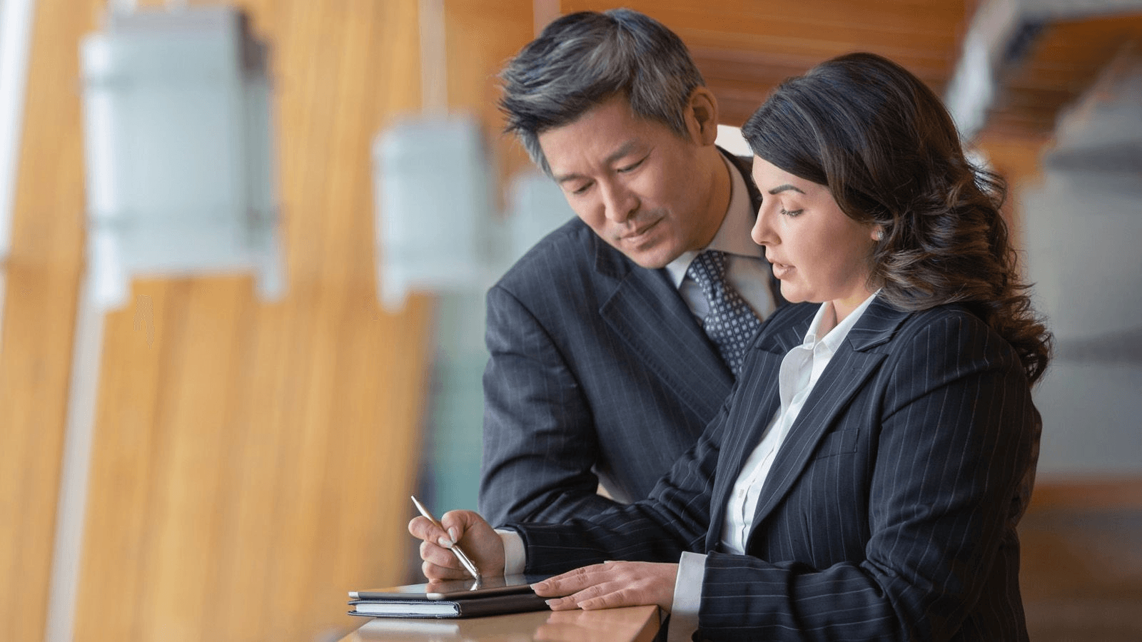 A man and a woman in business attire looking at a tablet, the woman using a stylus.