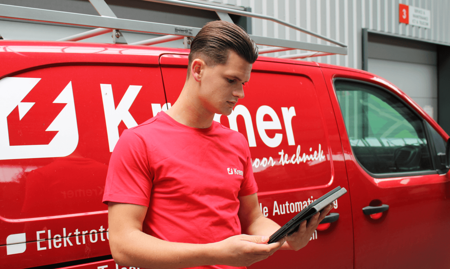Man in red shirt looking at tablet in front of company car.