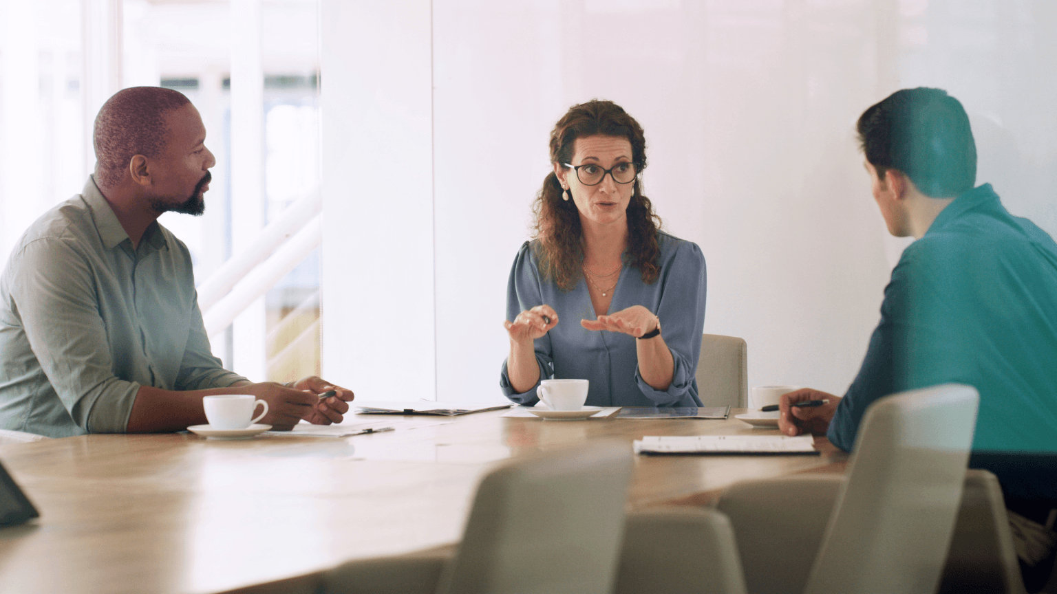 A woman speaks and gestures to two men during a meeting at a conference table.