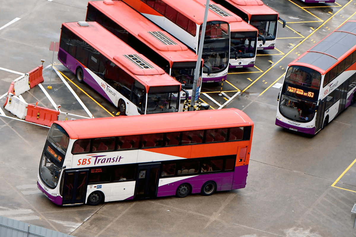 Multiple orange and purple SBS Transit buses, including double-deckers, parked in a paved lot.