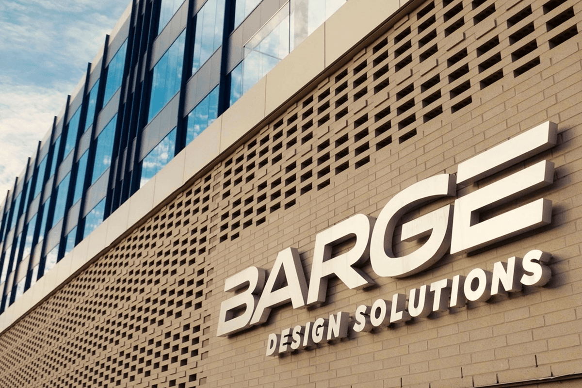 White "BARGE DESIGN SOLUTIONS" sign on a modern brick building with a glass upper facade.
