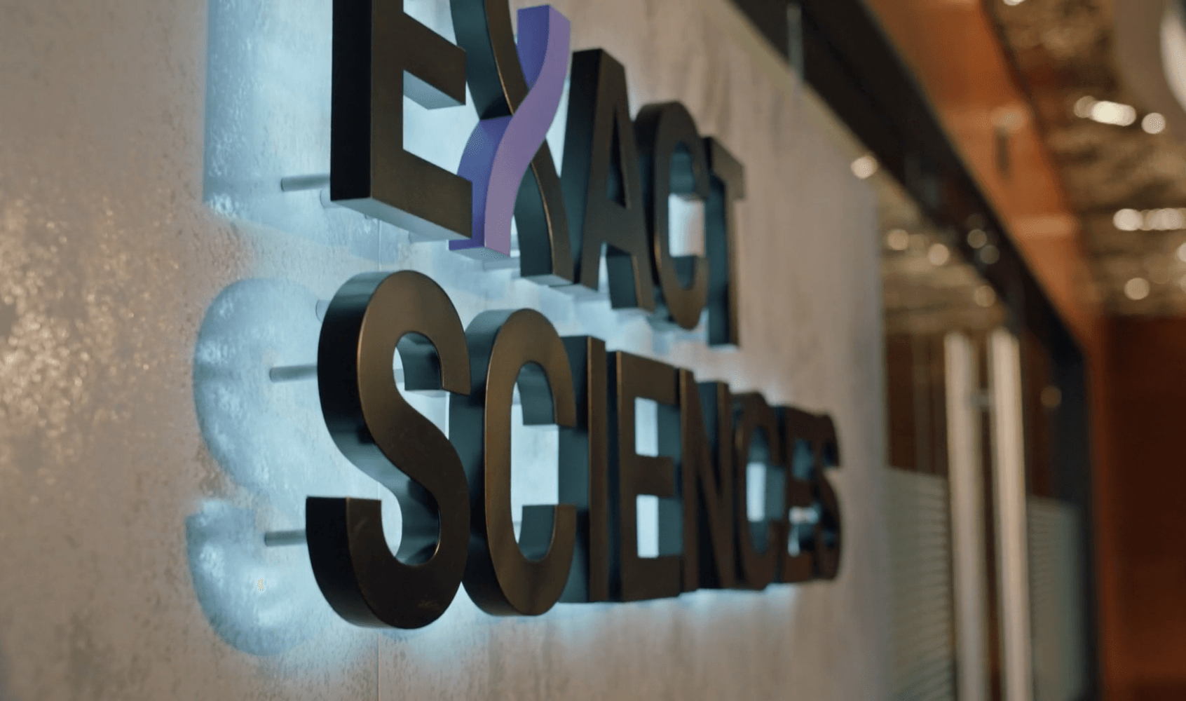 Backlit "EXACT SCIENCES" sign with a purple, stylized X.