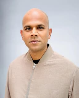 A bald man in a tan bomber jacket.