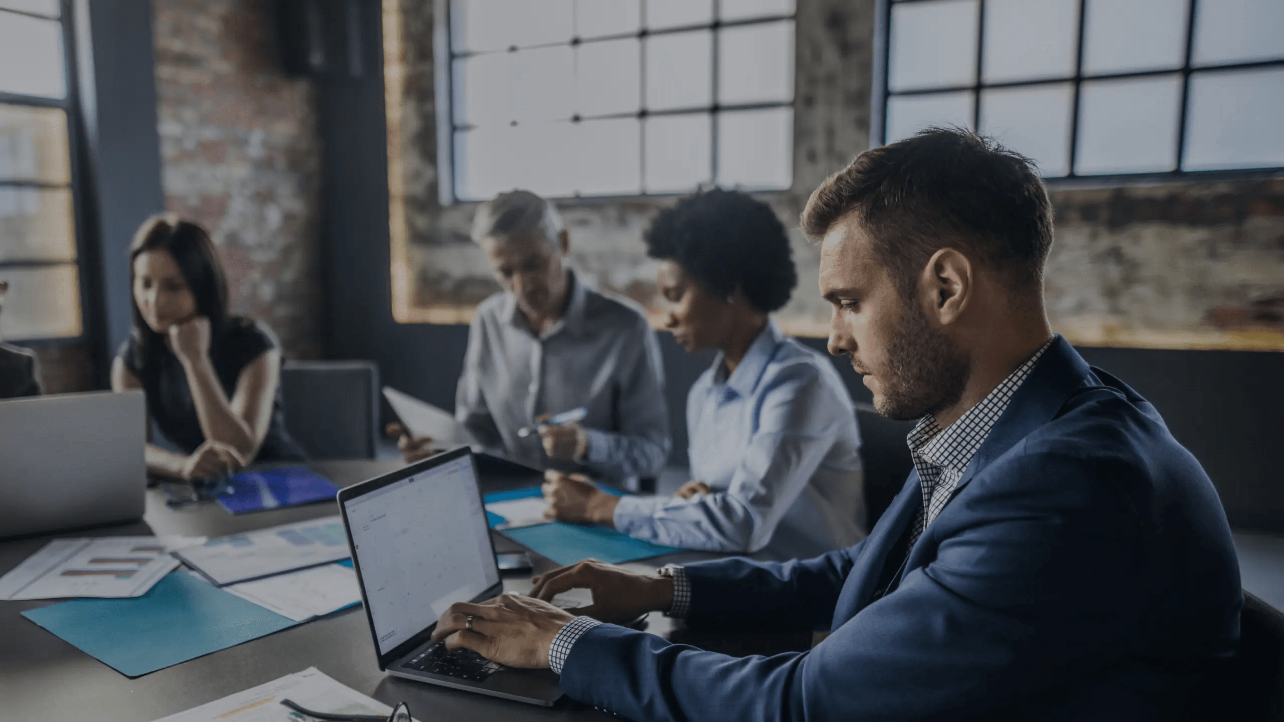 Four people sitting around table typing and looking at laptops.