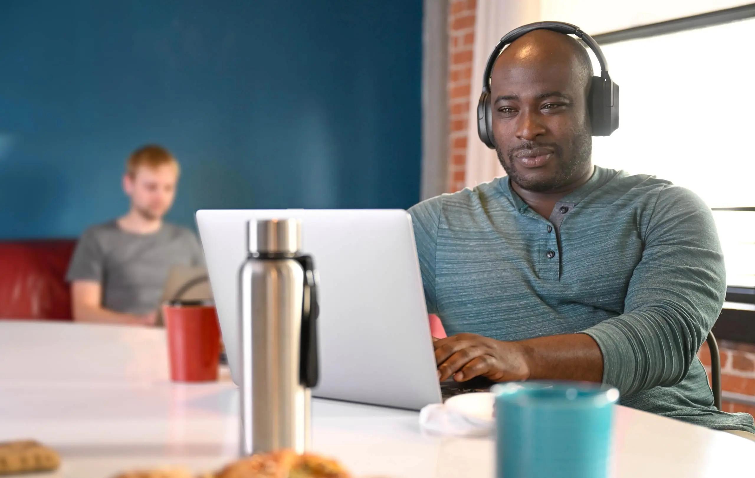 Image of a man smiling, wearing headphones while working at a laptop. This shows a modern learning experience you can achieve through Cornerstone.