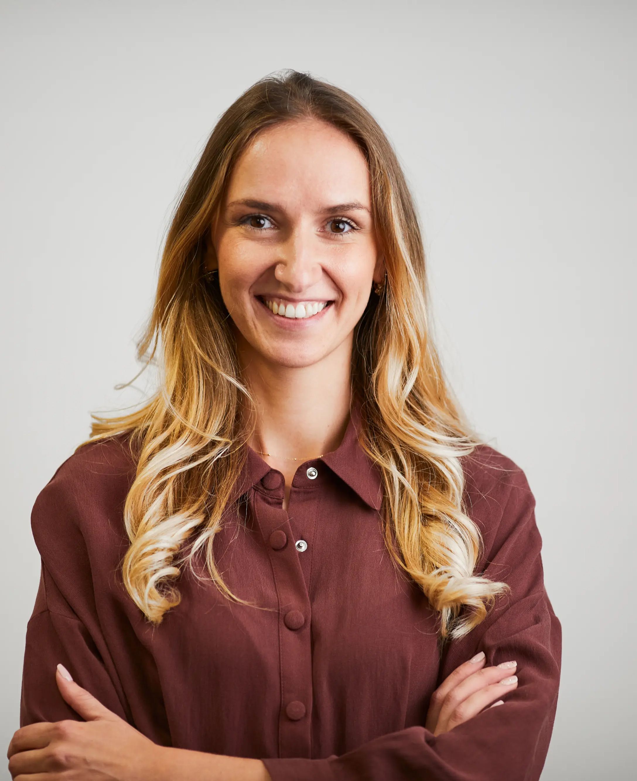 A woman in a maroon shirt is smiling with her arms crossed.